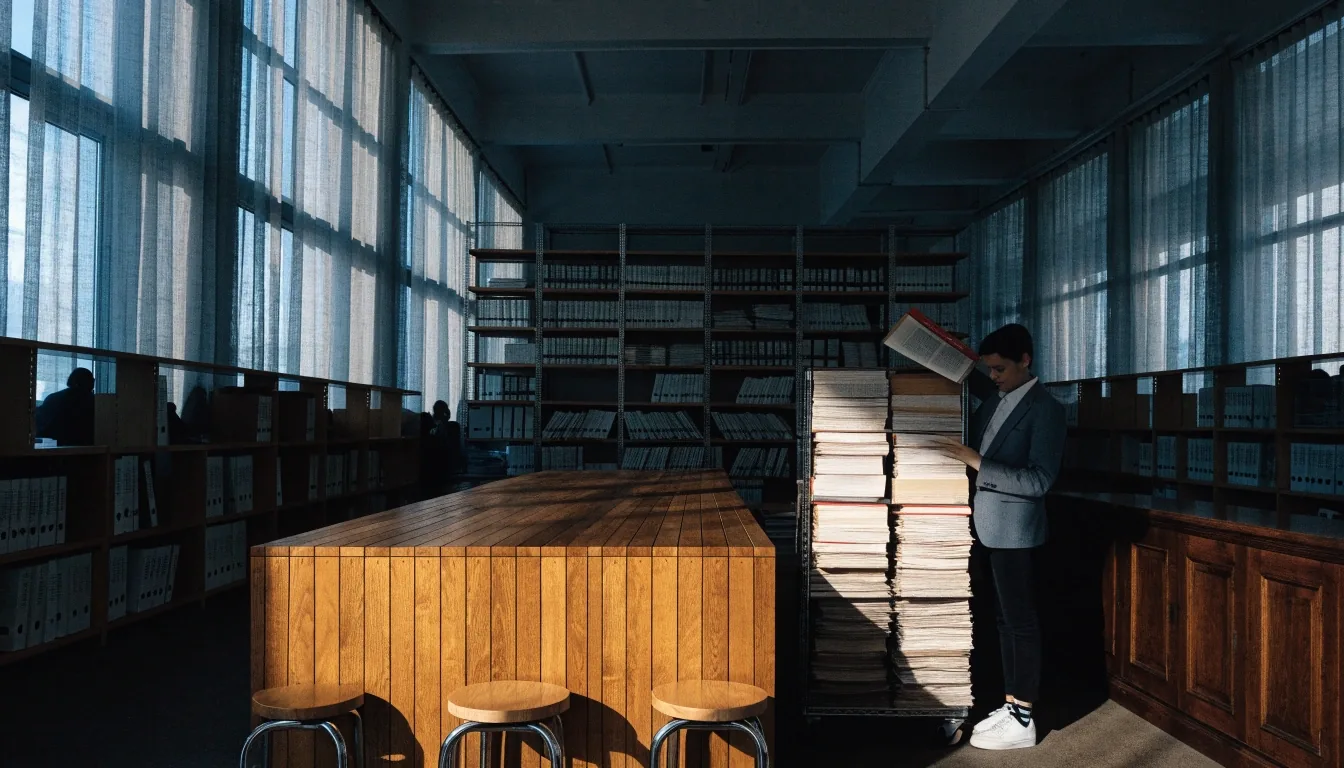An analyst working through a stack of loose-leaf policy volumes at a table in a quiet reference room