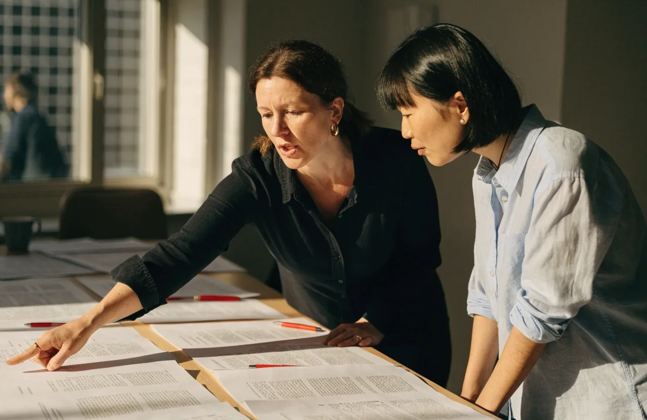 Two editors comparing printed page proofs during a plain-language review